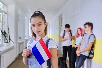 Student teenager girl with Netherlands flag inside school, school children group background