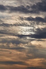 Sunset with dark clouds in the glowing sky, sun hiding behind layer of a clouds