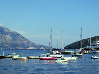 Fototapeta na wymiar Sailing yachts and motor boats on the water between a mountain and an island on the Budva Riviera in Montenegro
