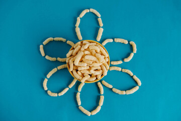 Corn sticks in a bowl in the shape of a flower on a blue background. Top view. Place for your text