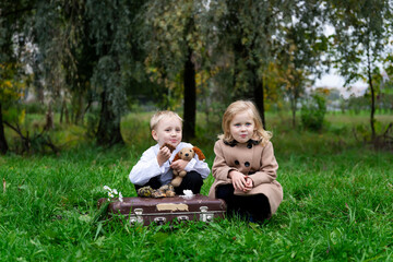 Little boy and girl dressed in retro clothes eat meager food on a retro suitcase. sitting on the grass.