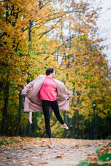 Woman ballerina in pointe shoes in golden autumn park, standing in beautiful pose on yellow leaves