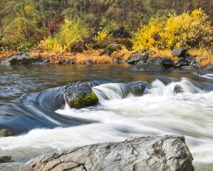 Autumn colors line the bank of the Trinity River while the water cascades over boulders.
