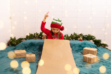 a little girl in a New Year's costume writes a wish list or a letter to Santa Kaus for Christmas....