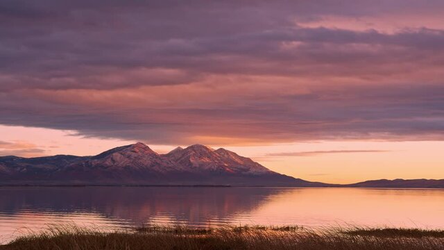Time lapse of clouds moving over Nebo Mountain reflecting in Utah Lake during colorful sunset.