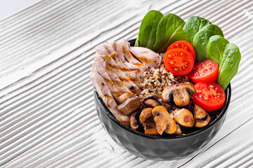 bowl of healthy quinoa with grilled chicken and vegetables on a white rustic wooden background