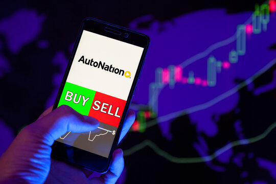 Company logo AUTONATION Inc. on smartphone screen, hand of trader holding mobile phone showing BUY or SELL on background of stock chart. Russia, Stavropol, - May 25, 2019
