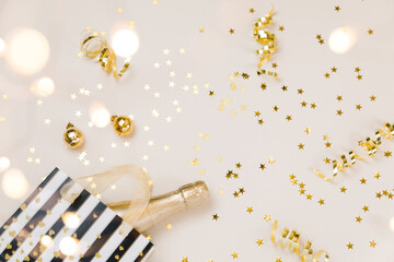 Festive gold background. Shining stars confetti, party streamers and decoration, holiday package on beige and Set Sail Champagne. Christmas. Wedding. Birthday. Flat lay, top view, copy space.