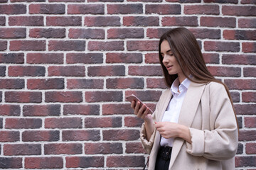 Fototapeta na wymiar A young woman looks at her phone. The brick background.