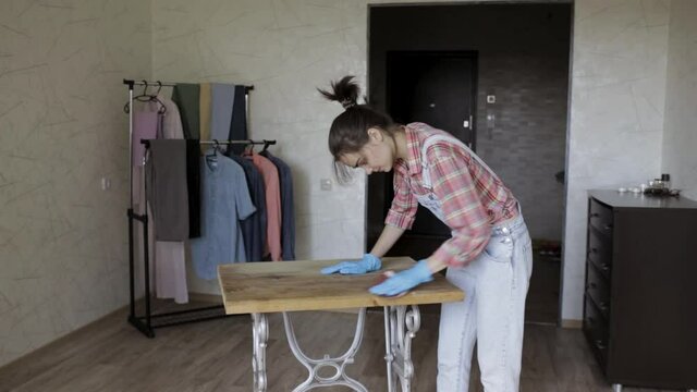 Smiling woman polishing wooden table with sandpaper while renewing furniture at home 