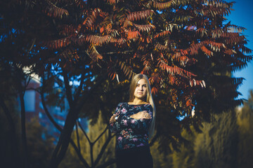 Woman girl long-haired blonde in a forest with trees with red leaves. She is happy confident in a...
