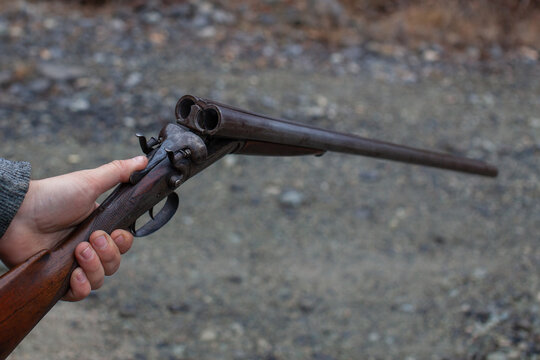 A man holds an old, antique, double-barrel break action shotgun out, ready to load two rounds into the bore. Outdoor range in Squamish, British-Columbia