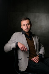 Studio portrait of a young caucasian man in a black blazer, looking at the camera, standing against plain studio background