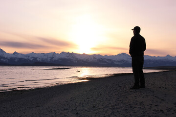 Fototapeta na wymiar Silhouette of Man on Eagle Beach on Lynn Canal Overlooking the Chilkat Mountain Range in Southeast Alaska