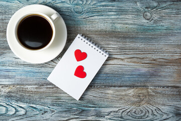 Romantic background with a Cup of coffee and two hearts on a Notepad on a wooden gray-blue background. The view from the top. The concept of Valentine's day.