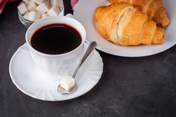 delicious fresh croissant and cup of coffee on a dark stone rustic background
