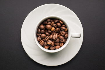 White coffee cup with coffee beans on a saucer, dark background