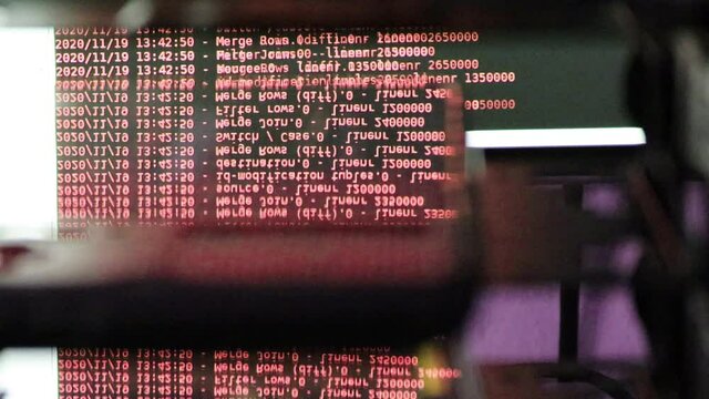 Red computer software code moving on a black monitor reflect on glass. Abstract computer hacking in process with rack server base, dynamic text running and flowing on pc screen