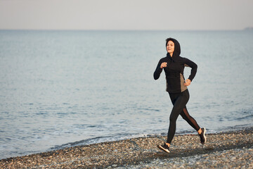 Caucasian woman in black sportswear enjoys a morning jogging on the beach, healthy lifestyle, outside running