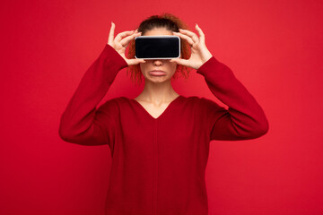 happy woman blinks eyes, with blank screen, shows modern device, isolated over red background. Technology concept