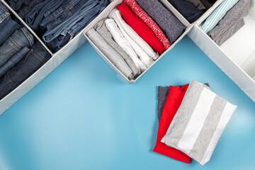 Vertical storage of clothing, tidying up, room cleaning concept. Stack of folded clothes in basket over light blue background. Top view