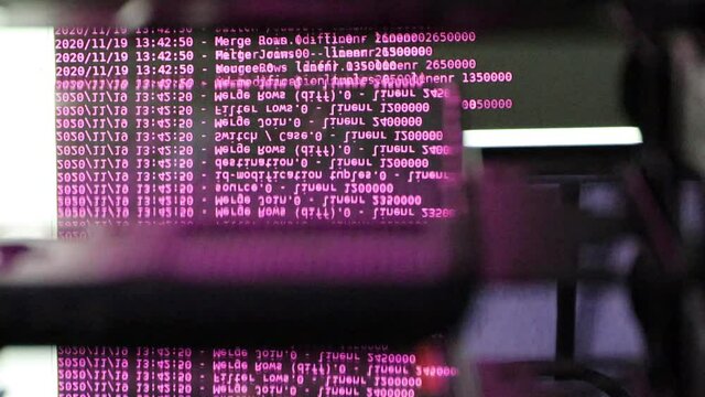 Pink computer software code moving on a black monitor reflect on glass. Abstract computer hacking in process with rack server base, dynamic text running and flowing on pc screen