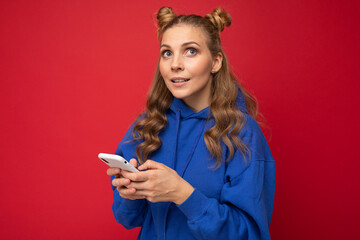 Naklejka premium Image of a thinking dreaming young beautiful woman posing isolated over red wall background using mobile phone.