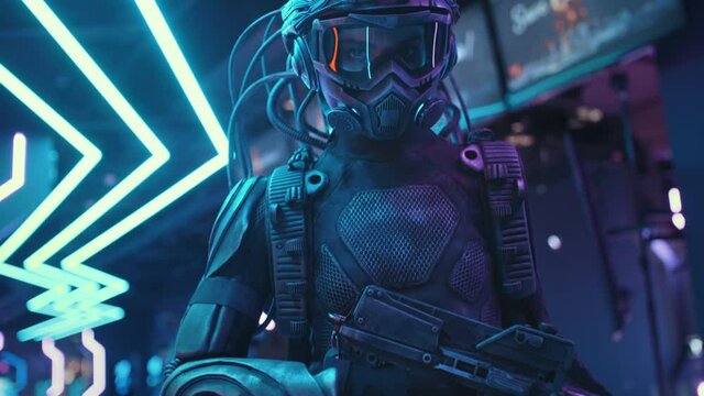 Female soldier of future in fiction helmet holding assault gun in her hands lit with blue neon street lights. Woman combat cyborg in futuristic protective costume. Cyberpunk warrior at night