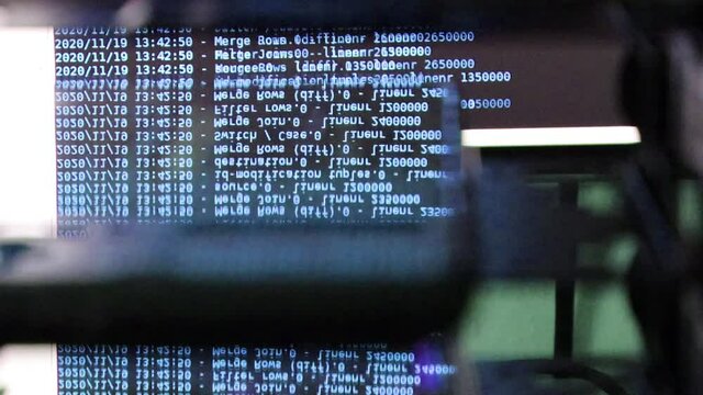 blue computer software code moving on a black monitor reflect on glass. Abstract computer hacking in process with rack server base, dynamic text running and flowing on pc screen