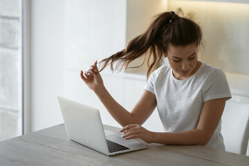 woman with a ponytail is typing text on a laptop computer sitting in the kitchen near a large window. make an application form in the Bank's website app for a loan remotely online from home.