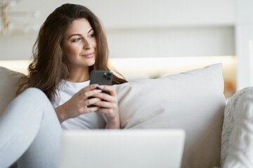 make an application form in the Bank's website app for a loan remotely online from home. beautiful woman of Caucasian appearance brunette typing text on the phone sitting in the living room 