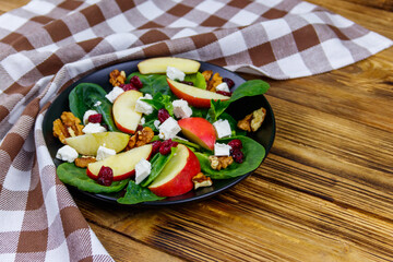 Autumn spinach salad with apple, feta cheese, walnut and dried cranberry on wooden table. Healthy vegetarian food