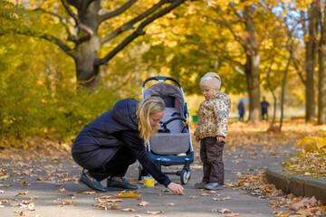 Happy family: mom and daughter draw on the asphalt with chalk in the autumn park. Fallen yellow-orange foliage of maples covers the ground. Sunny day. Outdoor games.