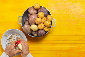 Man hands peeling three different potato types for colombian ajiaco over rustic yellow table