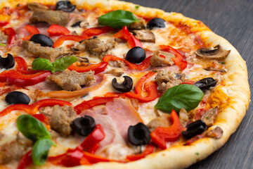 Italian pizza with melted mozzarella cheese, olives and sausage garnished with fresh vegetables and basil leaves