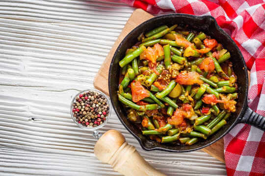 stewed green beans in a cast iron skillet on a white wooden rustic background