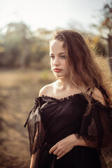 girl stands in the park in autumn in the rays of the setting sun