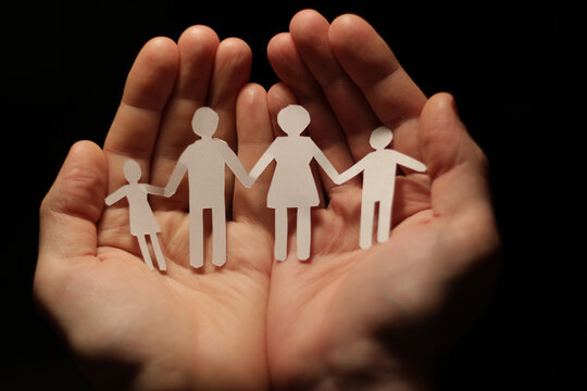 A cut out paper family holding hands, forming a chain, with cupped hands protection, safety, protection and care concept.