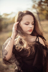 Naklejka premium girl stands in the park in autumn in the rays of the setting sun