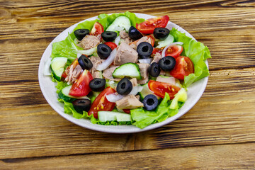 Tasty tuna salad with lettuce, black olives and fresh vegetables on wooden table