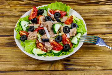 Tasty tuna salad with lettuce, black olives and fresh vegetables on wooden table