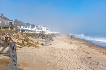 Person strolling along a sandy beach lined with holiday homes on a misty autumn morning, Seabrook,...