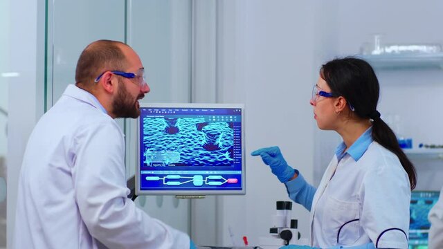Group of scientists working in modern equipped laboratory pointing on computer desktop. Team of doctors examining vaccine evolution using high tech researching diagnosis against covid19 virus