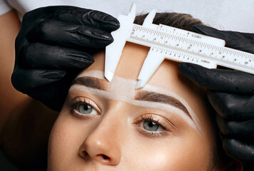 Cosmetician measuring brows before permanent makeup procedure