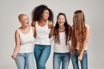 Portrait of four young diverse women wearing white shirts and denim jeans laughing together while...