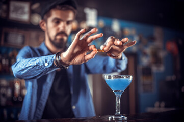 Bearded bartender places the finishing touches on a drink while standing near the bar counter in nightclub