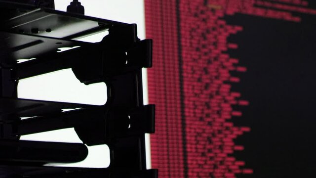 Red computer software code moving on a black monitor reflect on glass. Abstract computer hacking in process with rack server base, dynamic text running and flowing on pc screen