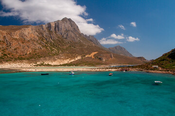 Fototapeta premium the surface of the clear sea and in the background is a mountain and blue sky with white clouds in Greece during the day and a sailing ship on the surface