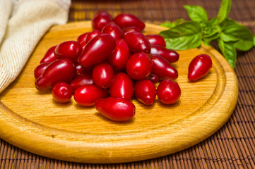 Still life - fresh large dogwood berries, purple plums and a sprig of basil on a wooden board