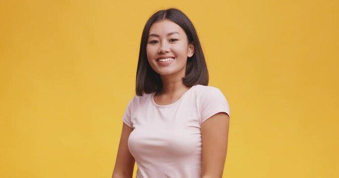 Studio portrait of young cute asian lady, preening hair and smiling to camera, orange background